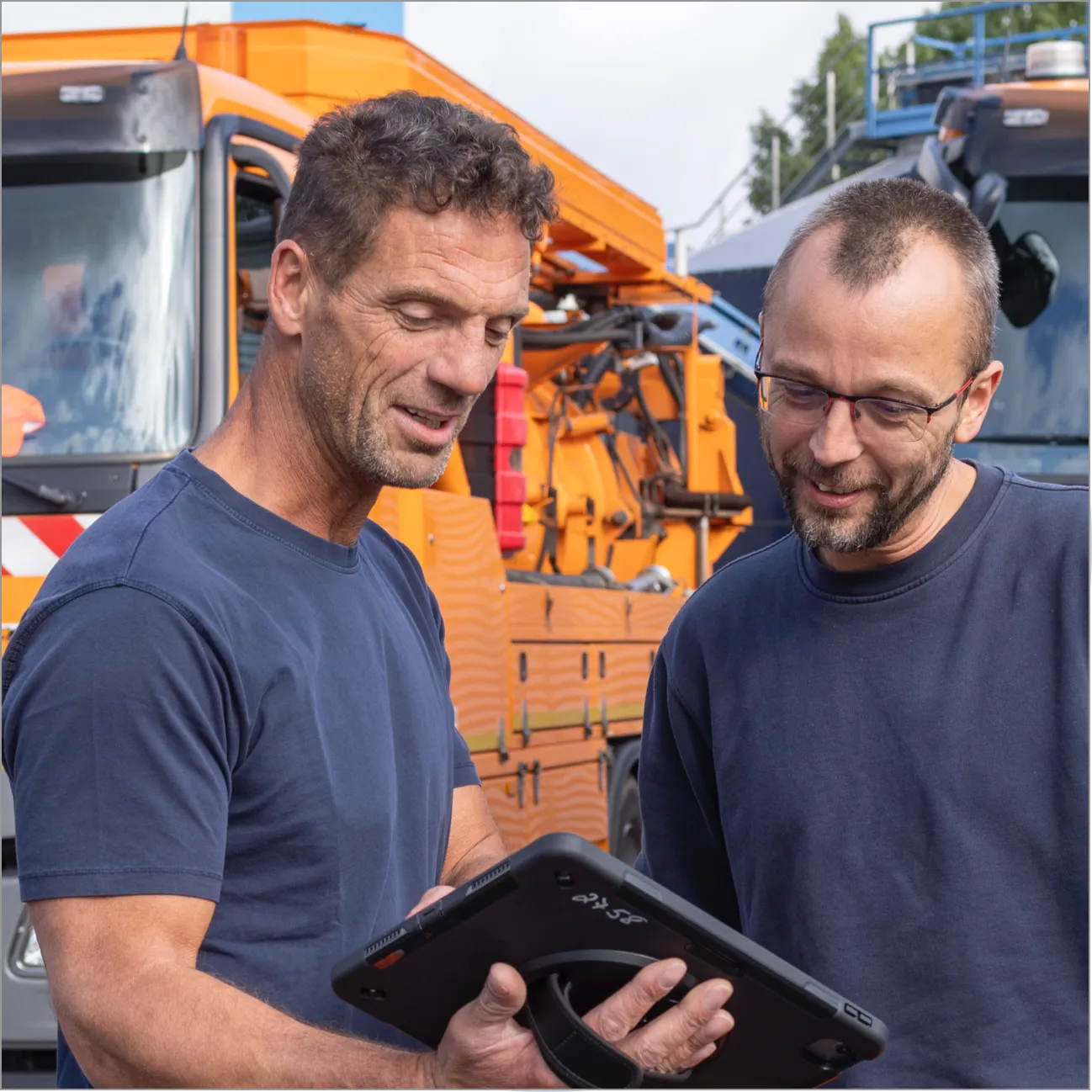 Zwei Mitarbeiter prüfen gemeinsam Daten auf einem Tablet vor einem Einsatzfahrzeug